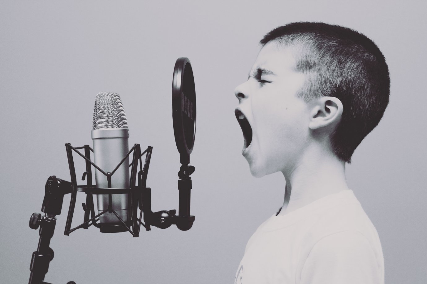Photo by Jason Rosewell on Unsplash A boy singing into a microphone that has a pop shield. He has his eyes closed and mouth wide open.