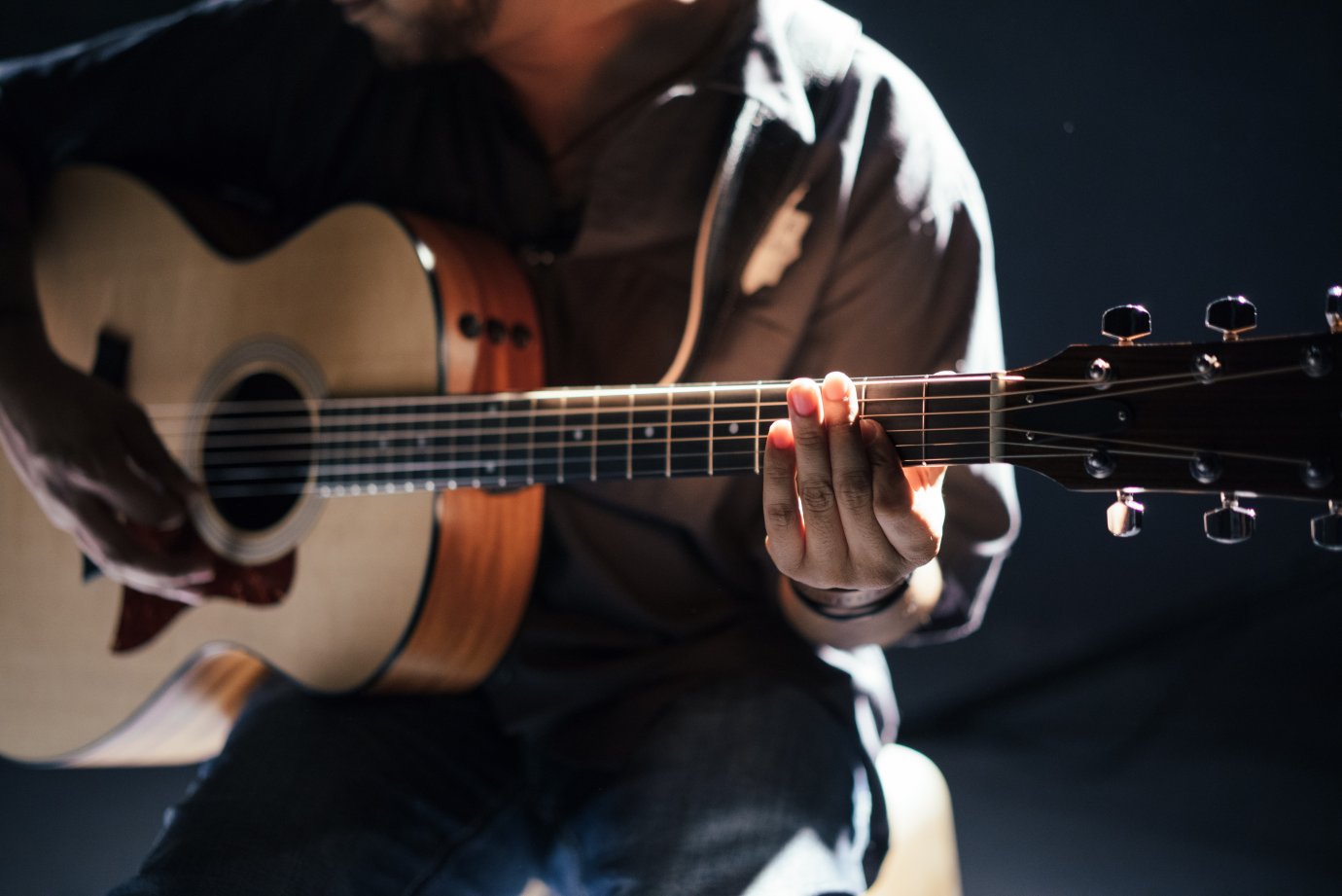 Man sat down playing an acoustic guitar. You can only see his torso.