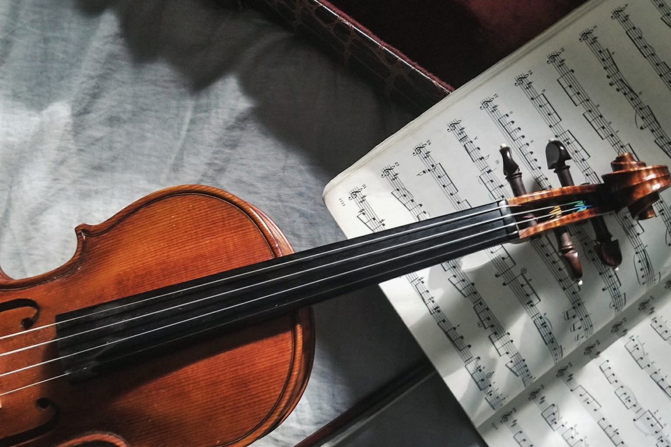 Photo by Jordan Mixson on Unsplash A violin laid on top of some sheet music, with the violin case at the top of the photo.