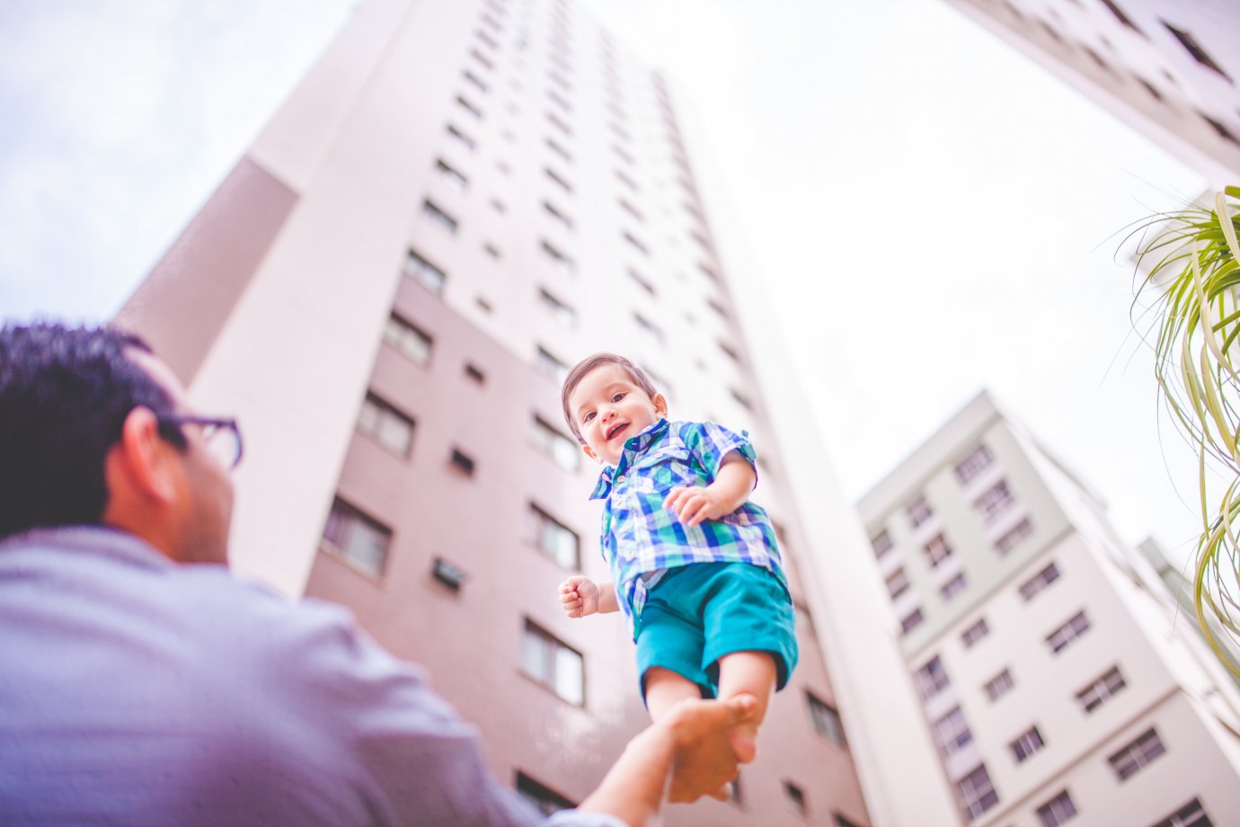 Father holding son up high with one hand. The child is looking at the camera and smiling.